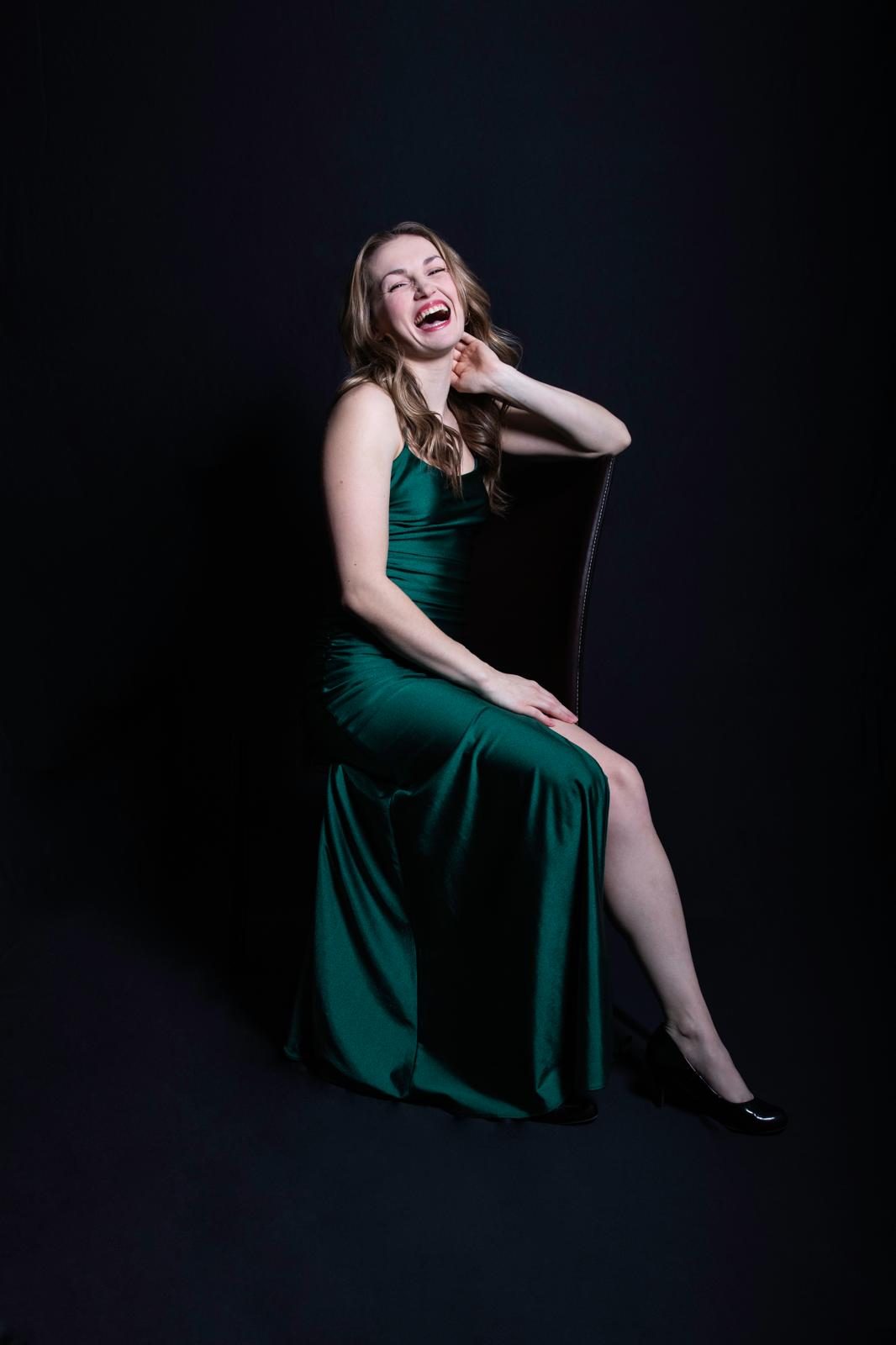 Paige Robinson laughing, seated in a green satin gown against black