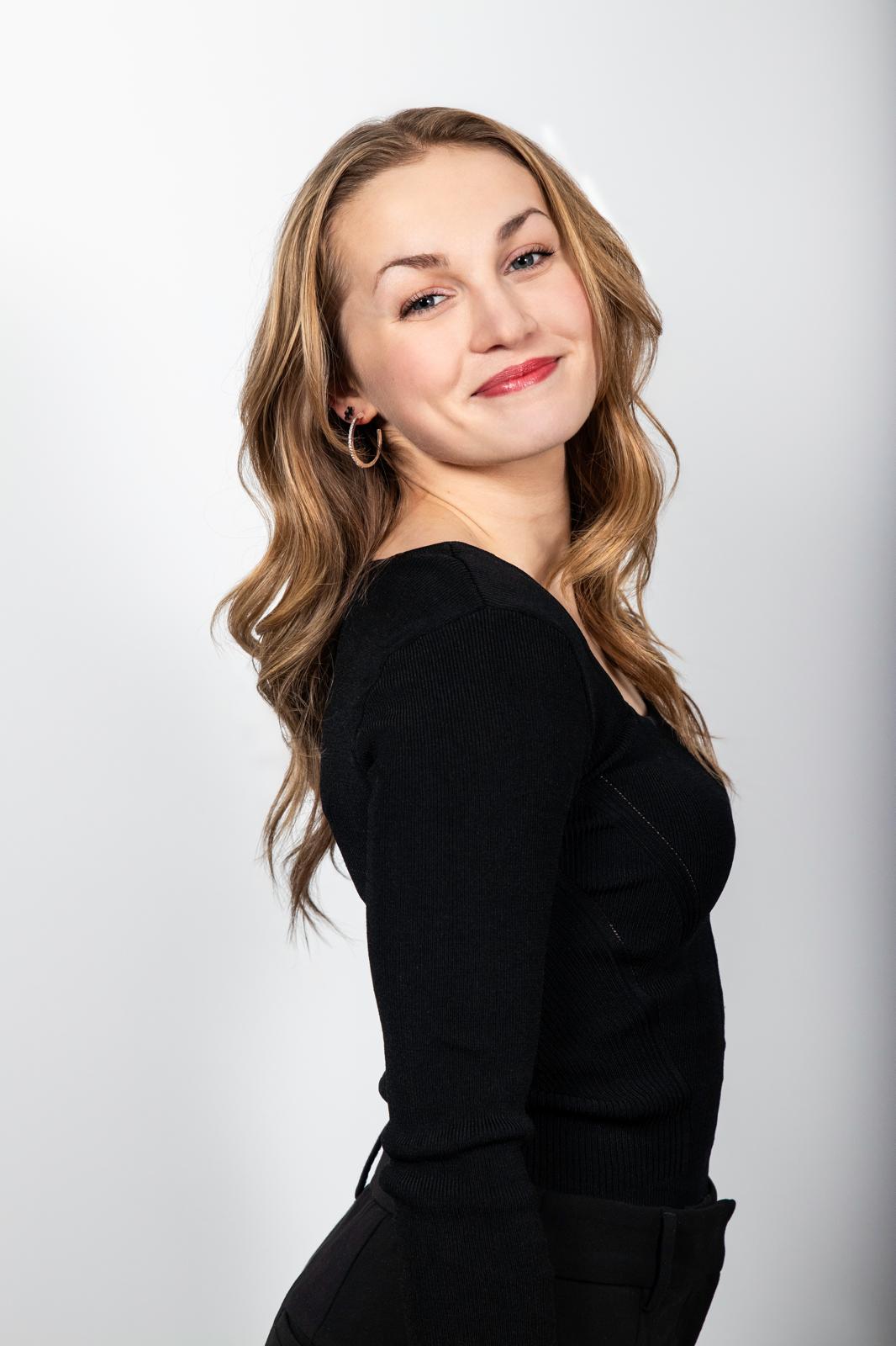 Paige Robinson smiling over her shoulder, in black, on a pale grey backdrop